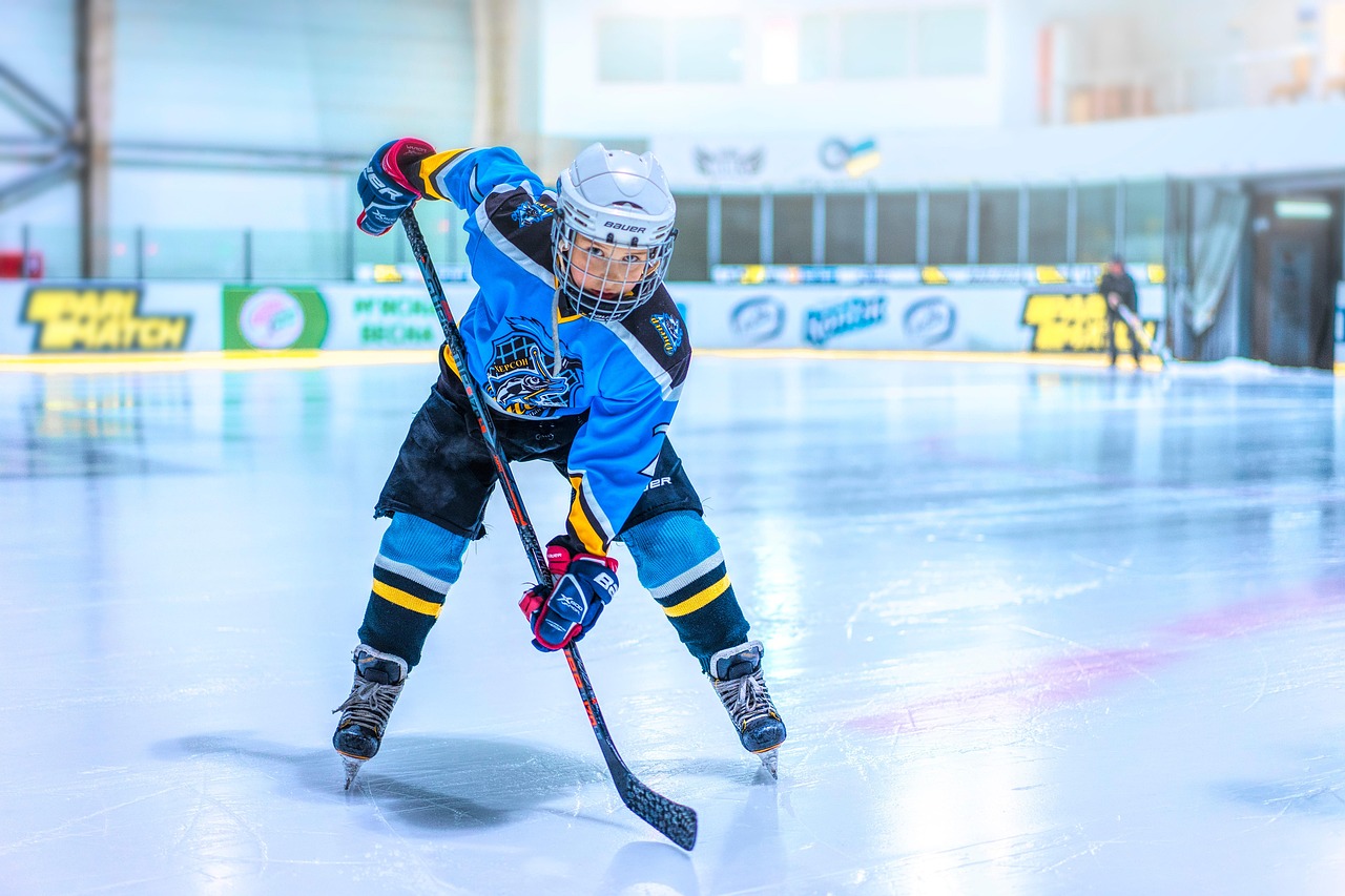 Young ice hockey player in blue jersey skating with stick raised on rink